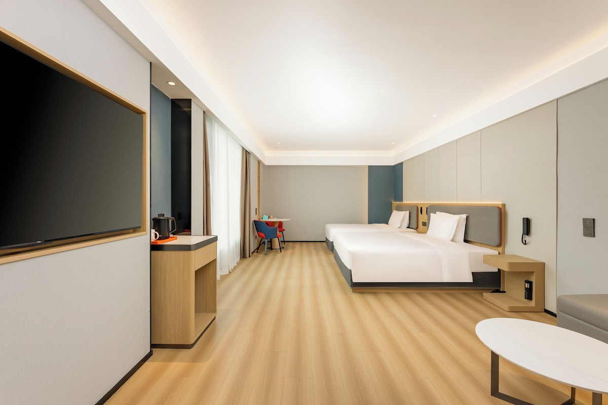 A modern hotel room with a large bed, a desk, a chair, and a TV.