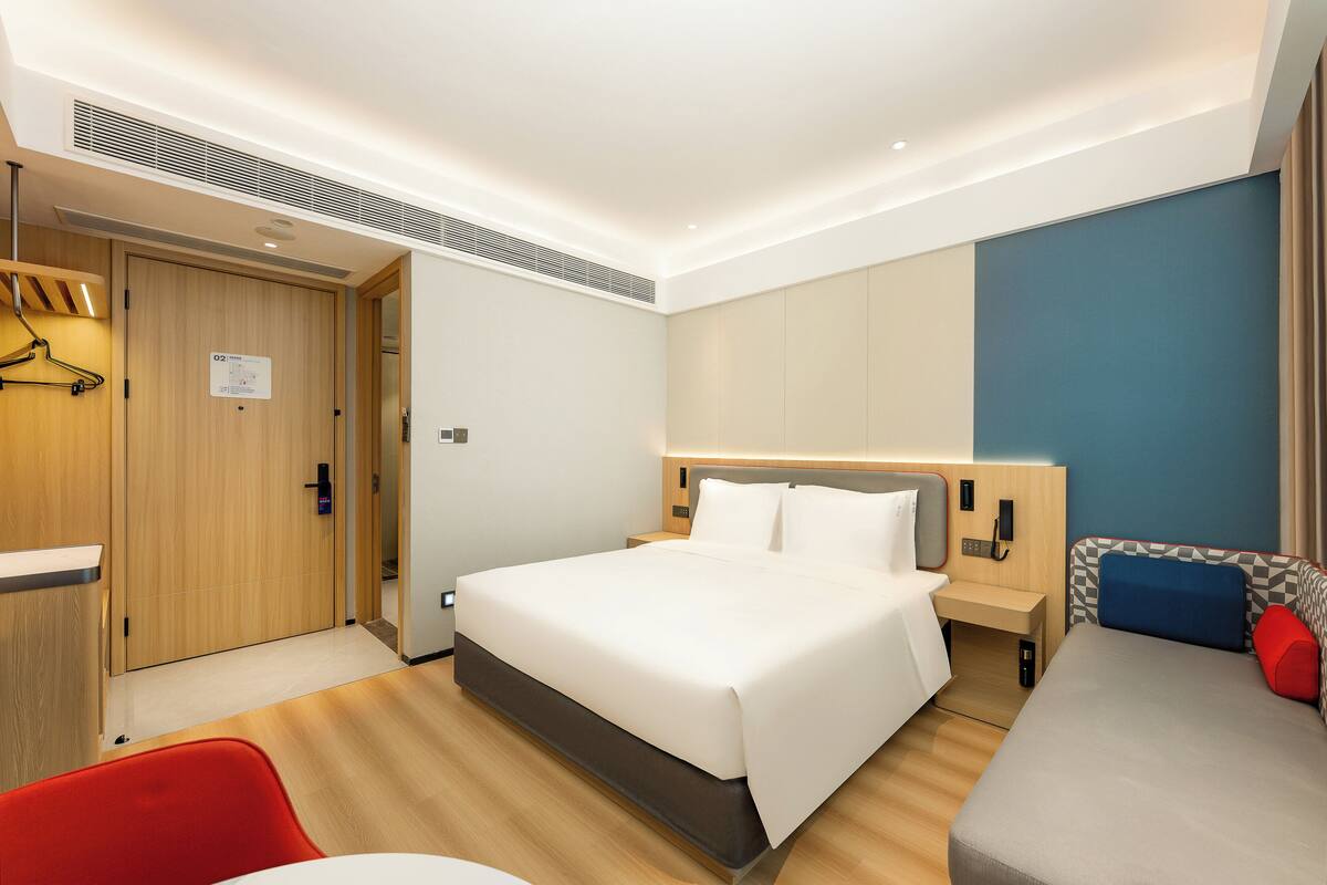A modern hotel room with a large bed, bedside tables, a desk, a chair, and a sofa.