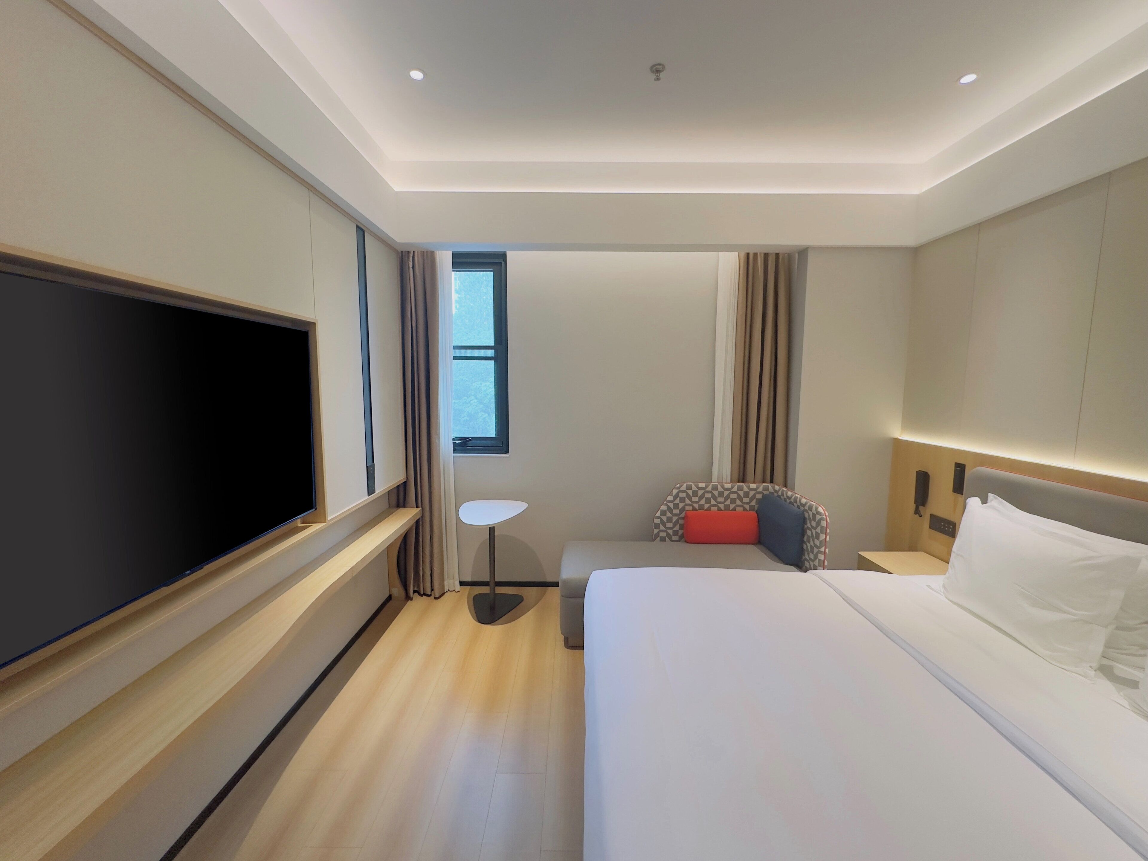 Habitación de hotel con una cama grande, televisión de pantalla plana, una mesita y una ventana con cortinas.