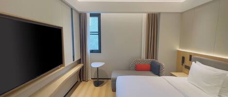Habitación de hotel con una cama grande, televisión de pantalla plana, una mesita y una ventana con cortinas.