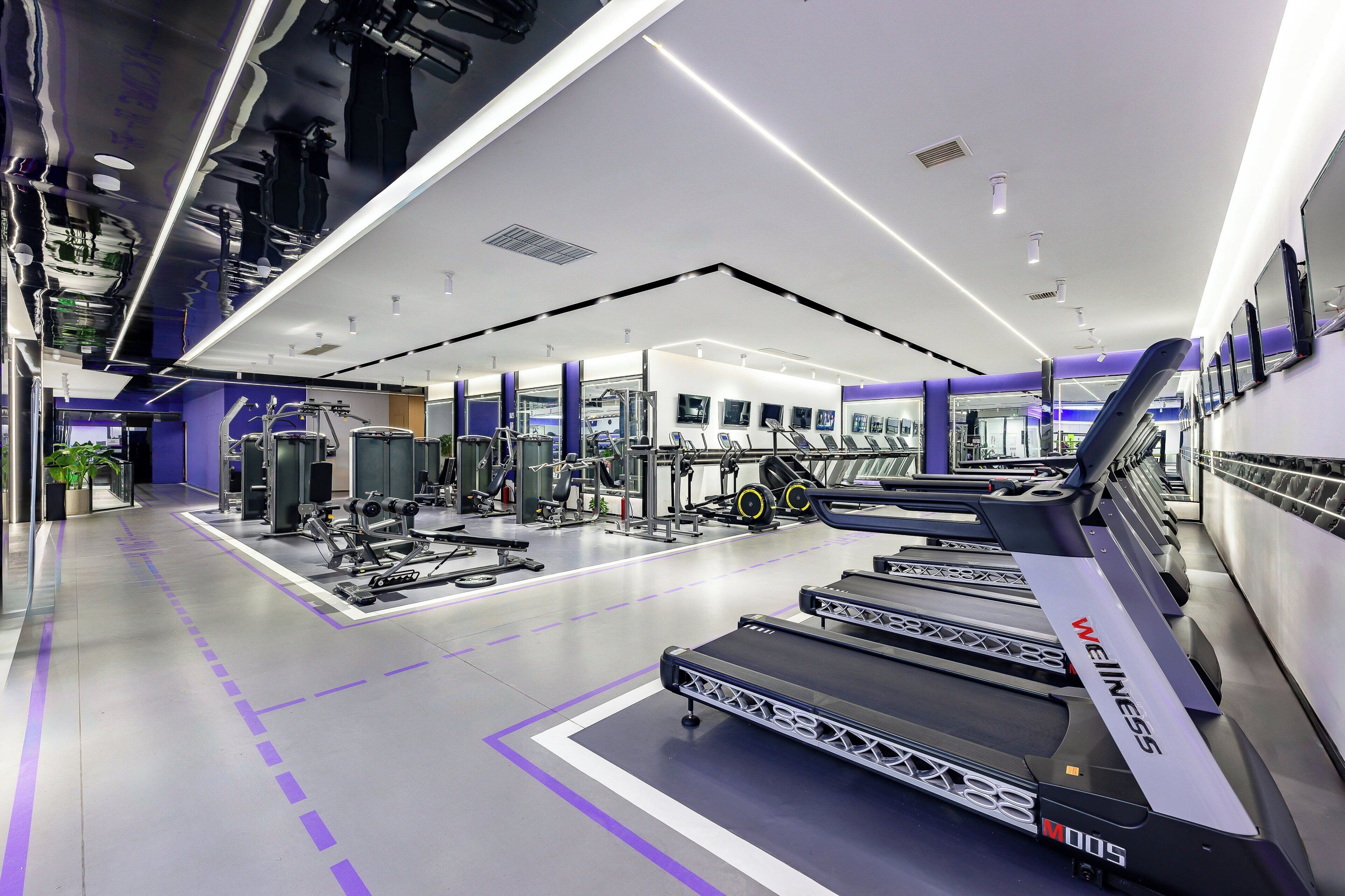 Un gimnasio moderno con cintas de correr, máquinas de pesas y un espejo grande.