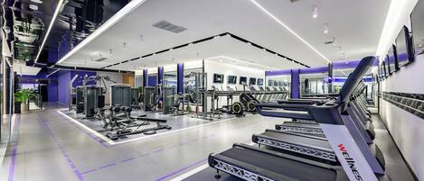 Una palestra moderna con tapis roulant, macchinari per pesi e uno specchio lungo una parete.
