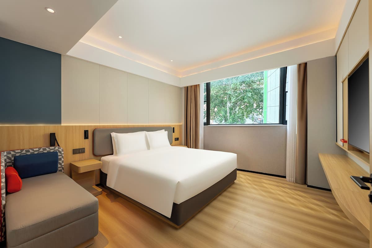 A modern hotel room with a large bed, a sofa, a TV, and a window with curtains.