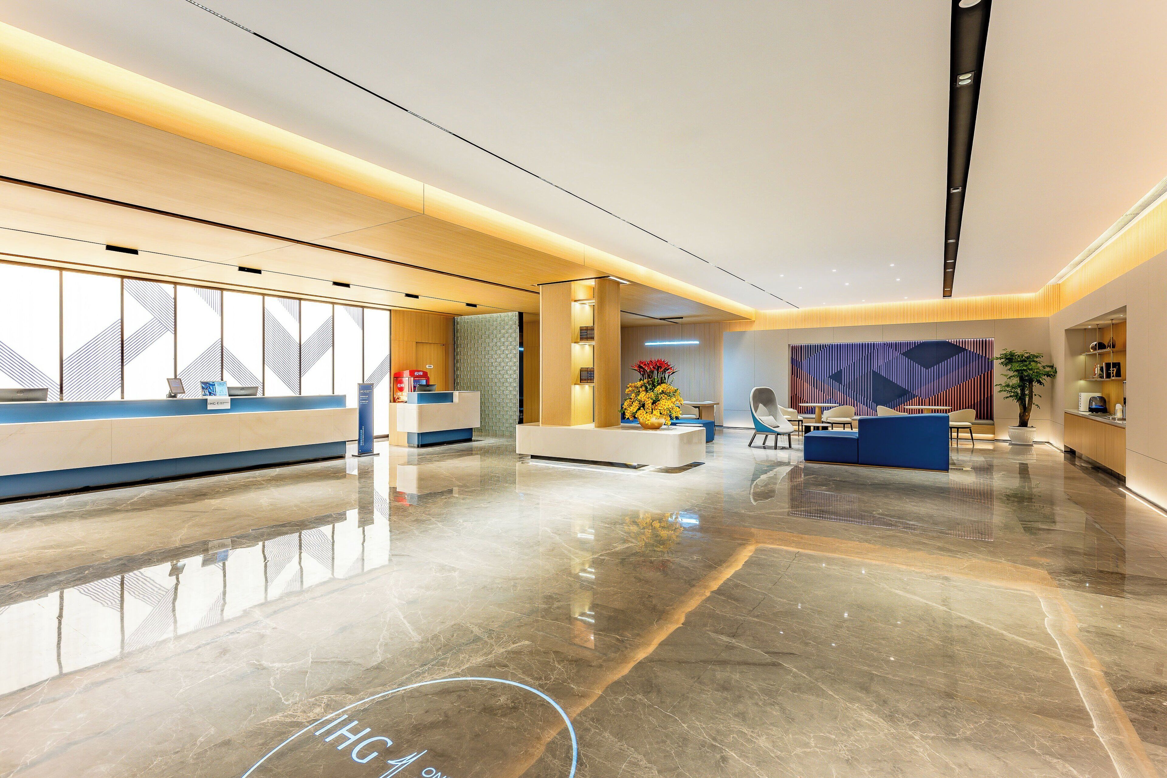 A modern hotel lobby with a reception desk, seating area, and a large window.