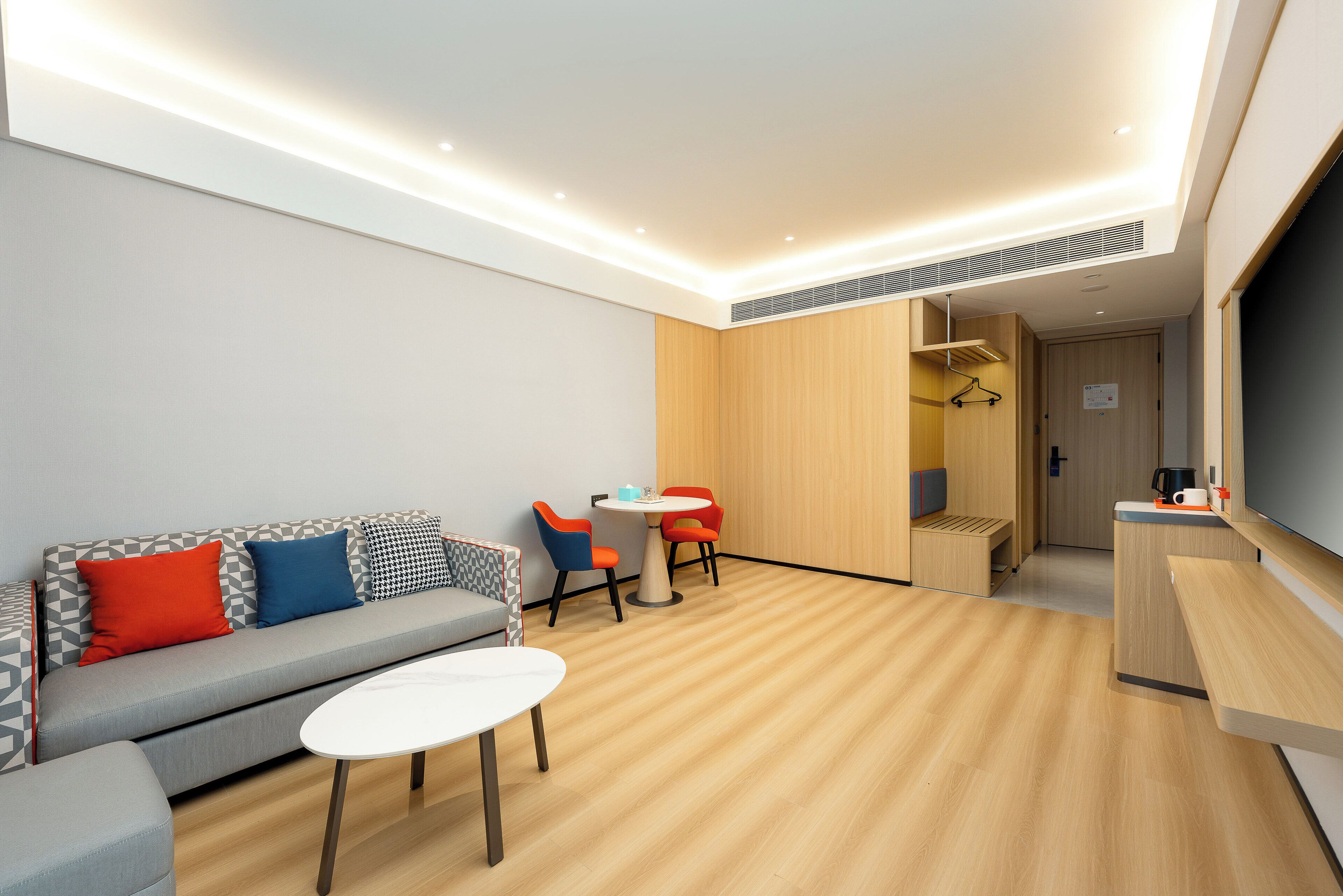A modern hotel room with a sofa, a small table, and a kitchenette area.