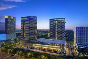 Un hotel de gran altura con fachada moderna, señalización llamativa de 'Holiday Inn Express' y 'Crowne Plaza', y un edificio inferior bien iluminado.
