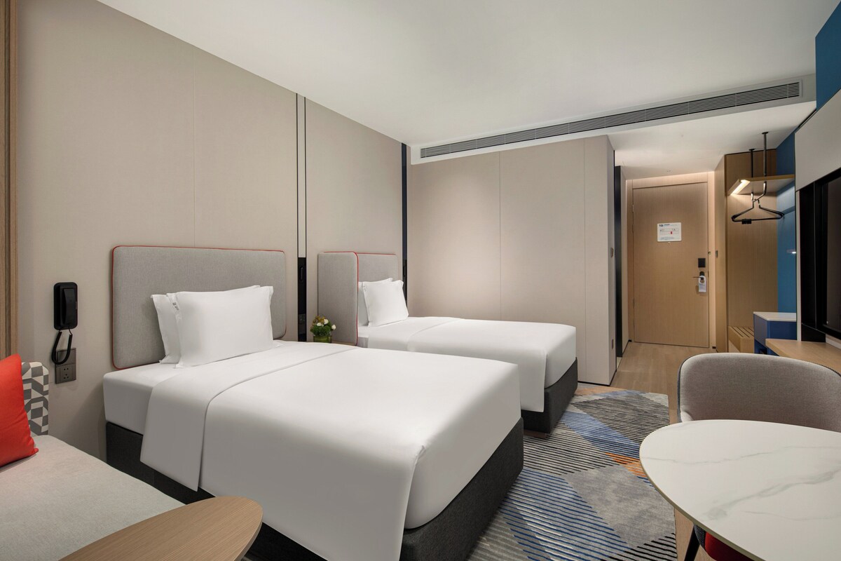 Een hotelkamer met twee bedden, een bureau, een stoel en een badkamers deur.