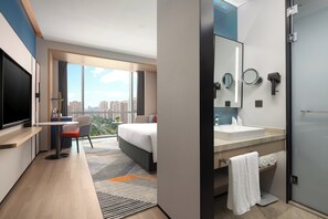 A modern hotel room with a large bed, a desk with a chair, a television, a bathroom with a sink and mirror, and a city view. - Holiday Inn Express Suzhou East Taihu by IHG (Suzhou)
