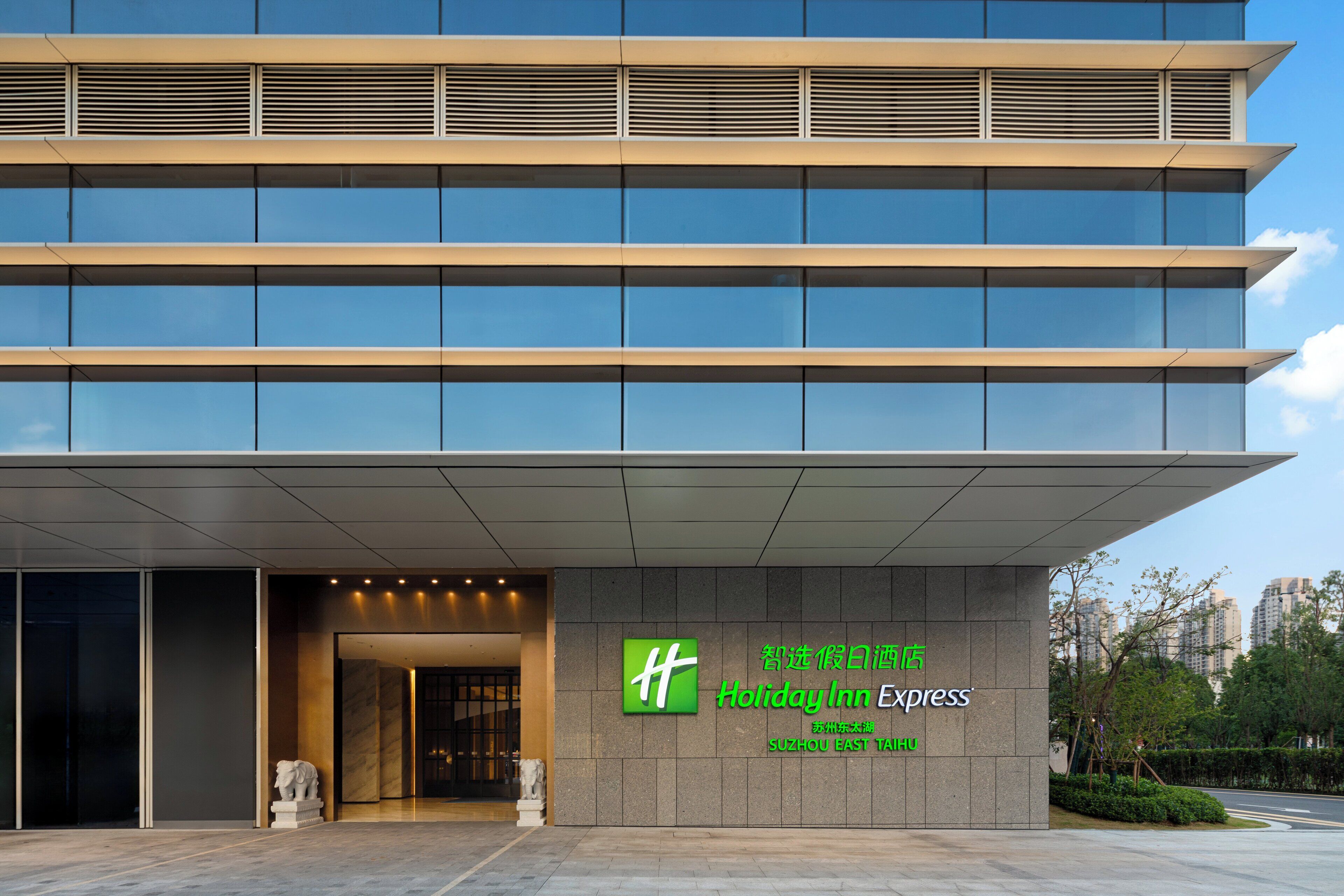 A modern hotel building with a large glass facade and a prominent green logo.