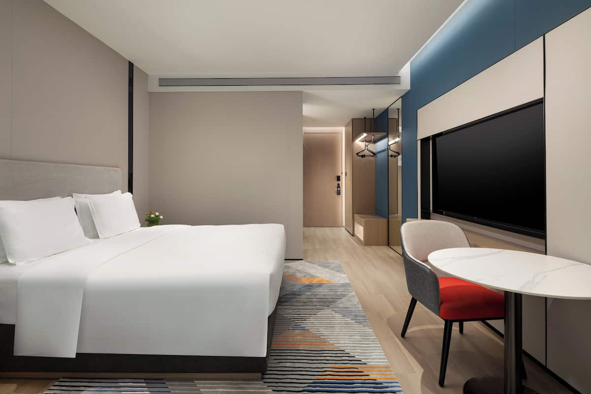 A modern hotel room with a large bed, a small table, a chair, and a TV.