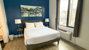 A bedroom with a bed, two bedside tables, a window with curtains, a radiator, and a blue accent wall. - 2BR apt near EWR airport 7xw8 (Elizabeth)