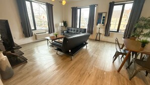 A modern living room with a black leather sofa, wooden dining table, and a TV on a stand. - 2BR apt near EWR airport 7xw8 (Elizabeth)