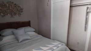 Ein Schlafzimmer mit Bett, Kissen, einer gemusterten Decke, einem Kleiderschrank und einer Wanddekoration.