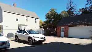 Eine Wohnstraße mit zwei parkenden Autos, einem weißen SUV und einer weißen Limousine, vor einem Haus mit einer Garage, auf der 'MICATROTTO' steht.