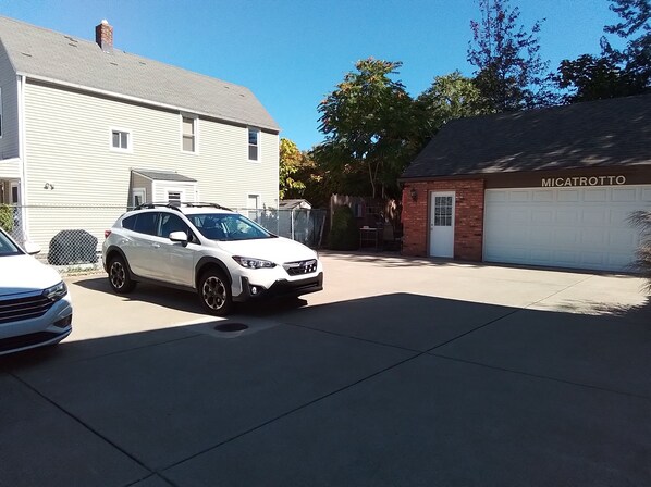 A residential street with two parked cars, a white SUV and a white sedan, in front of a house with a garage labeled "MICATROTTO".