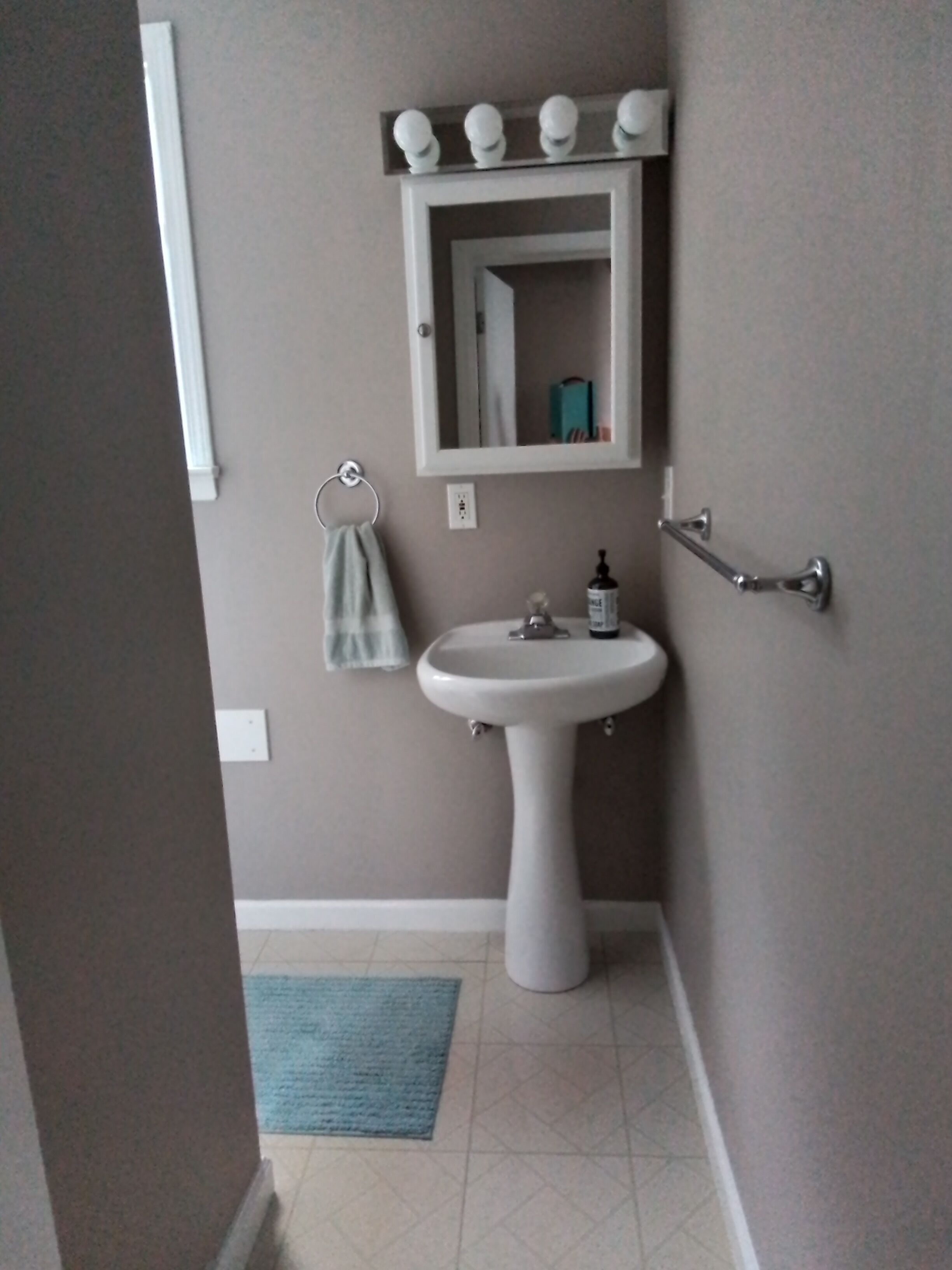 Une salle de bain avec un lavabo sur colonne, un miroir et un porte-serviettes.