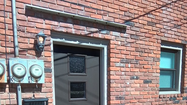 Ein Backsteinhaus mit grauer Tür, einem Fenster und elektrischen Kästen an der Wand.
