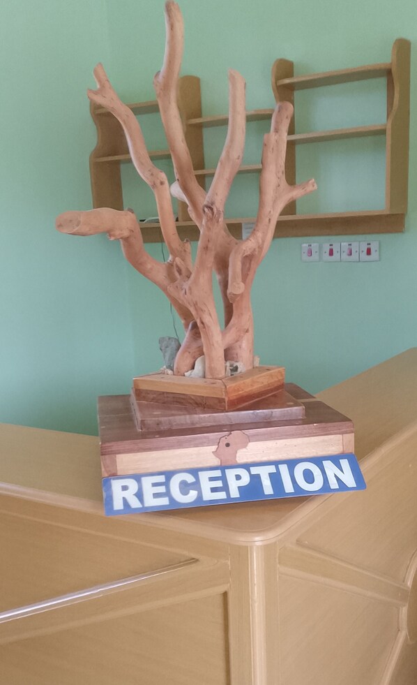 A reception desk with a wooden tree sculpture and a sign that reads "RECEPTION". - Elegance Lodge &Hotel (Serengeti)