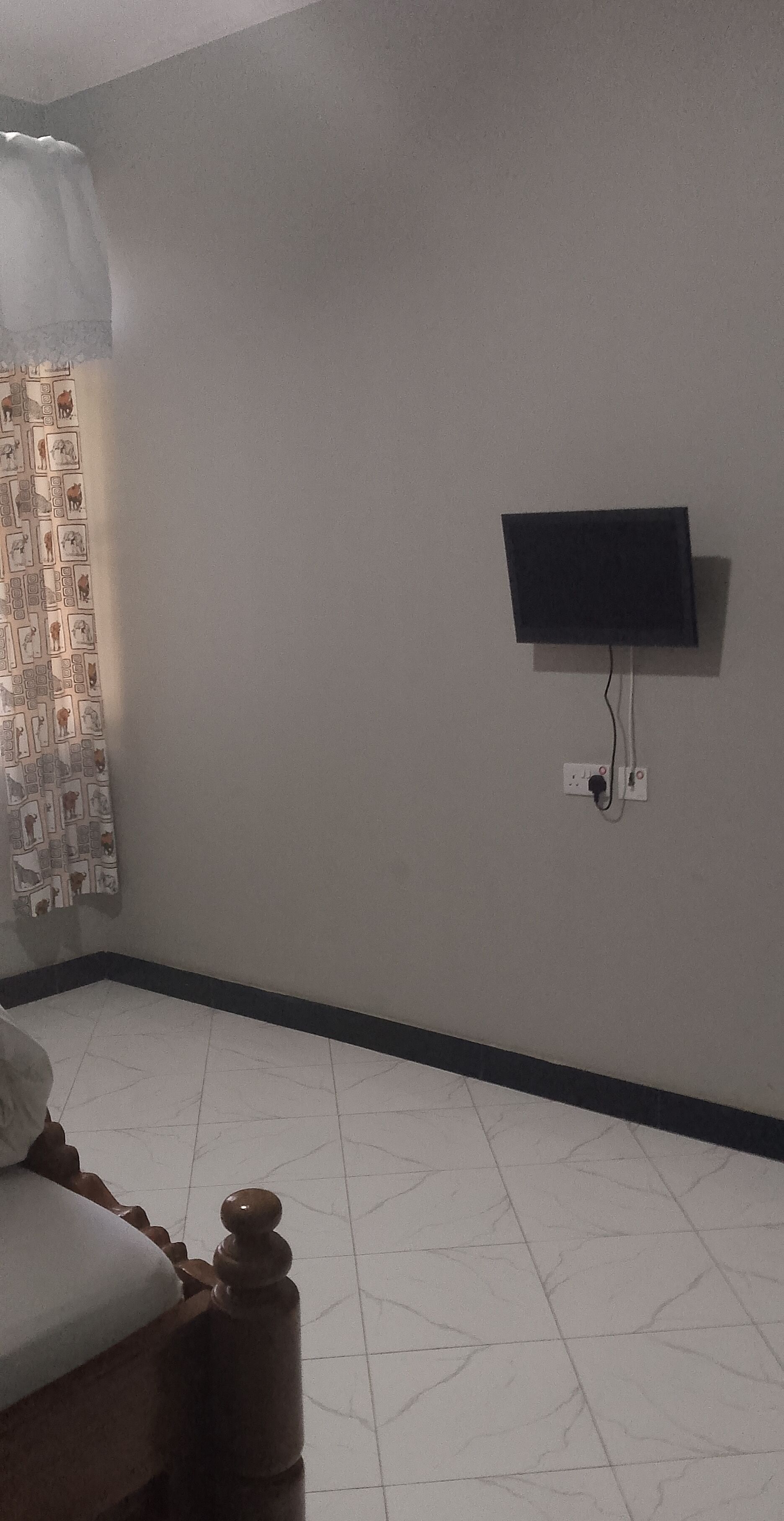 Ein Zimmer mit einem Bett, einem an der Wand befestigten Fernseher und einem Vorhang mit Muster.