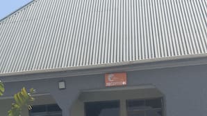 A building with a corrugated metal roof, a reception area, and a paved entrance with patterned tiles.