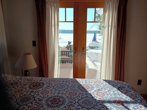 Un dormitorio con cama, lámpara y vista a un paisaje nevado a través de una puerta de madera.