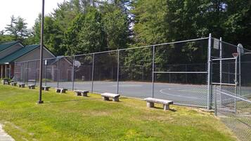 An outdoor basketball court with a chain-link fence, benches, and a building in the background.
