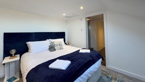 A modern bedroom with a large bed, a nightstand, a bedside lamp, and a view of a bathroom through an open door. - Perfect location for beach and golfing (Troon)