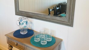 Una mesa de madera con un espejo encima, un posavasos azul, una jarra de vidrio y cuatro vasos.