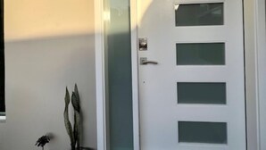 A white door with frosted glass panels and a metal handle. There are three potted plants to the left of the door. - CASA LIBERTAD 854 (Tijuana)