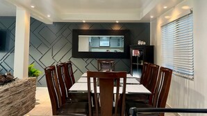 A modern dining area with a rectangular table and six chairs, a stone accent wall, a built-in TV, and a window with blinds. - CASA LIBERTAD 854 (Tijuana)