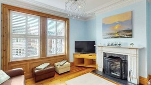 Ein Wohnzimmer mit Kamin, Fernseher, Sofa und einem Gemälde von einem Sonnenuntergang.