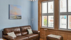 Ein braunes Ledersofa mit Kissen, ein kleiner Holztisch und ein Fenster mit Jalousien.