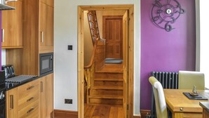 Eine Küche mit Holzausbau, einer Mikrowelle und einem Herd. Eine Treppe führt zu einem Raum mit lila Wand und einer dekorativen Uhr.