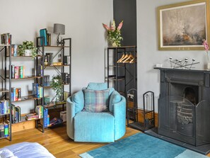 A living room with a blue armchair, a fireplace, a bookshelf, and a painting on the wall.