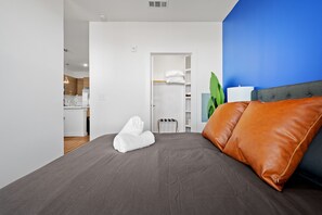 Ein modernes Schlafzimmer mit grauem Bett, braunen Lederkissen, einer blauen Akzentwand und einem weißen Kleiderschrank.