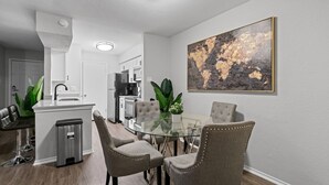 Moderni keittiö, jossa on valkoiset kaapit, musta jääkaappi ja lasinen ruokapöytä sekä neljä tuolia.