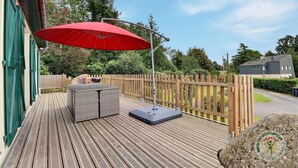 A wooden deck with a red umbrella, outdoor seating, and a view of a residential area. - The Villa in the country (PARIGNE)