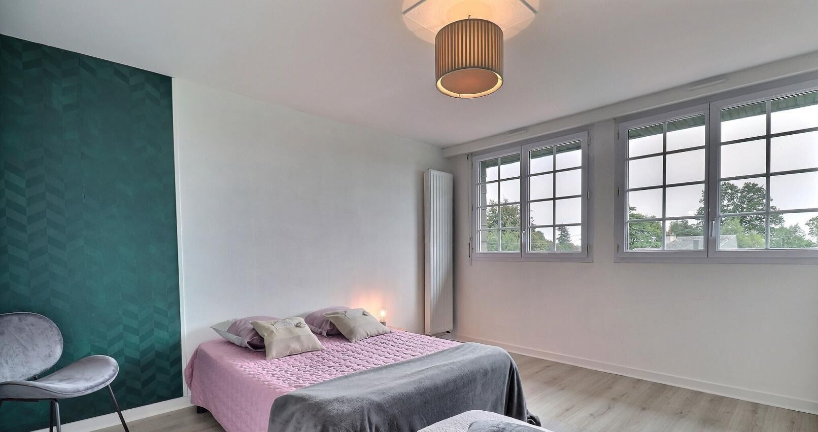 Een slaapkamer met een bed, een stoel en grote ramen.