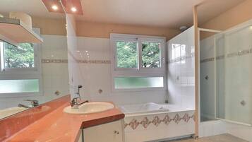 A bathroom with a sink, mirror, window, bathtub, and shower.