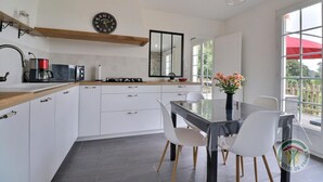 A modern kitchen with white cabinets, a wooden countertop, a gas stove, and a large window with a view of greenery. - The Villa in the country (PARIGNE)