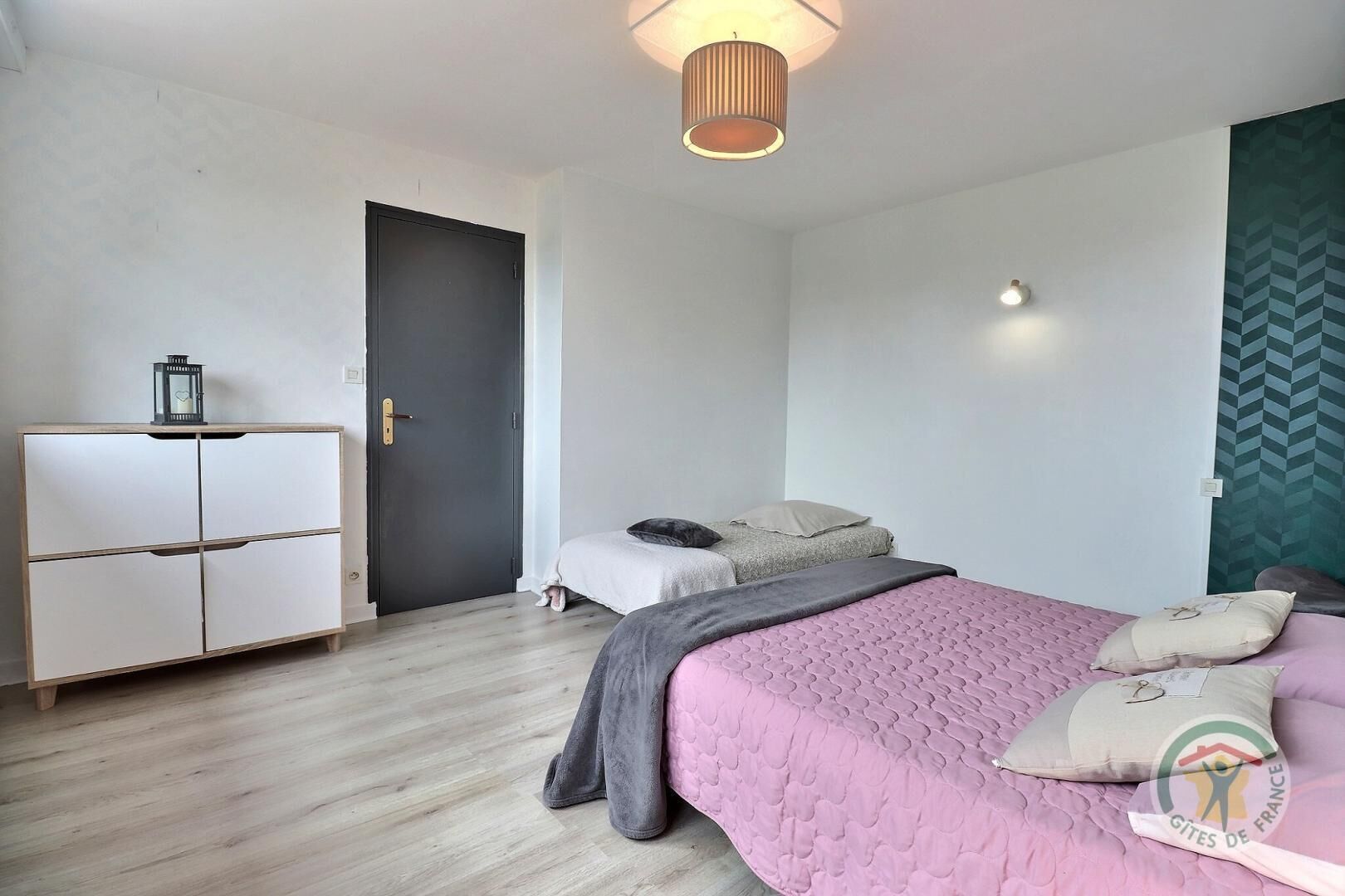 Une chambre à coucher comprenant un lit, une armoire, une porte et un mur orné d’un motif géométrique.