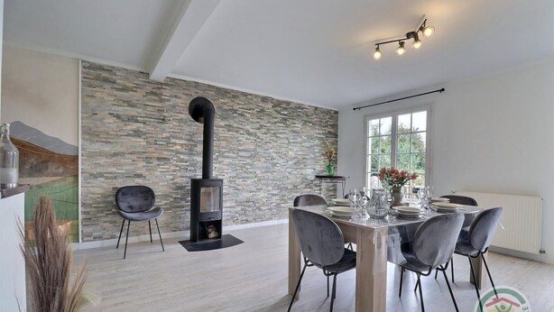 A modern dining area with a stone wall, a black wood-burning stove, and a table set for six. - The Villa in the country (PARIGNE)