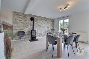 A modern dining area with a stone wall, a black wood-burning stove, and a table set for six.