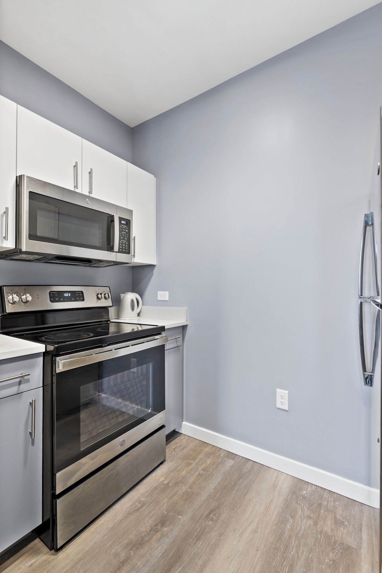 A modern kitchen with stainless steel appliances, including a microwave, oven, and refrigerator, against a light grey wall.