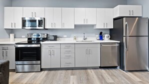 A modern kitchen with stainless steel appliances, white cabinetry, and a grey floor. - Cozy 1BR Near Encore Boston 7jk4 (Everett)