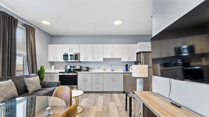 A modern kitchen with white cabinets, stainless steel appliances, and a dining area with a glass table and chairs. - Cozy 1BR Near Encore Boston 7jk4 (Everett)