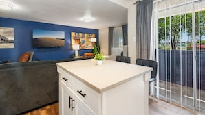 A modern kitchen with a central island, a dining area with a table and chairs, and a large sliding glass door leading to a balcony. - Beautiful Studio in University Hills v3tc (Austin)