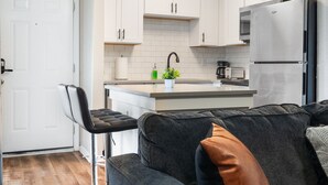 A modern kitchen with white cabinets, a stainless steel refrigerator, and a bar stool. - Beautiful Studio in University Hills v3tc (Austin)