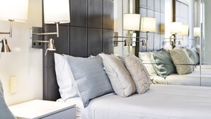 Ein modernes Hotelzimmer mit einem großen Bett, mehreren Kissen, einem Nachttisch und Wandlampen.