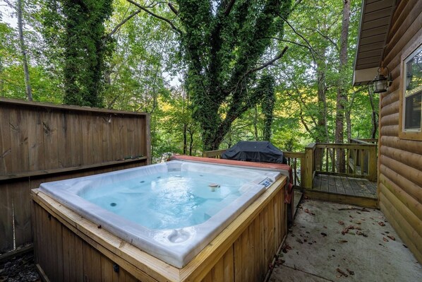 A hot tub in a wooded backyard with a wooden deck and a covered grill area. - A Little River Romance | Private Dock + Hot Tub (Mentone)
